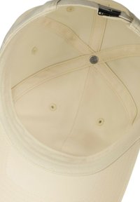 Interior de gorra beige con un forro de tela suave y cuatro orificios de ventilación, que presenta un botón central y una correa ajustable.