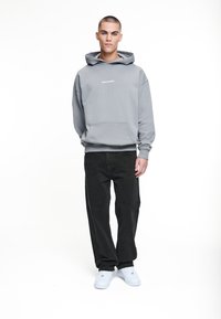 Grauer Hoodie mit Fronttasche und "PEGADOR"-Schriftzug, kombiniert mit schwarzen Hosen und weißen Sneakern. Einfaches, lässiges Design.