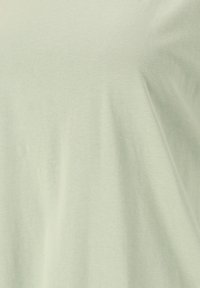 Ljusgrön kortärmad topp i mjukt, texturerat tyg med lös passform, på tape en rund halsringning och slät yta.