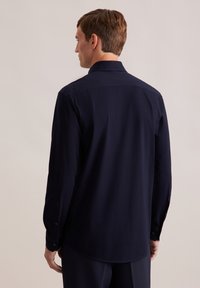 Camicia a maniche lunghe blu navy, tessuto morbido, collo standard, orlo leggermente curvo, polsini con bottone singolo, design minimalista. Vista laterale.