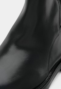 Gros plan sur une botte en cuir noir poli avec des coutures détaillées le long du côté et du bord de la semelle.