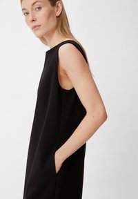Schwarzes ärmelloses Kleid mit hohem Kragen, seitlichen Taschen und glatter Textur. Einfaches, minimalistisches Design mit lockerer Passform.