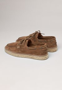 Bateaux en suede brun avec des semelles en jute tressé, dotés d'œillets et de lacets métalliques, conçus pour un look décontracté avec un talon découvert.