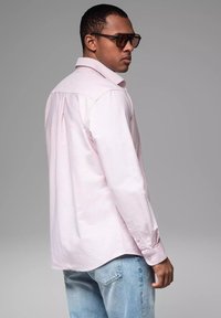 Lichtroze langemouwen shirt met een kraag, knoopdetails en een rechte zoom, gecombineerd met lichtblauwe jeans. Smooth stof textuur.