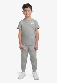 Siva bombažna majica s kratkimi rokavi in belim logotipom Nike, v kombinaciji s sivimi jogger hlačami in belimi supergami. Gladka tekstura, sproščen kroj.