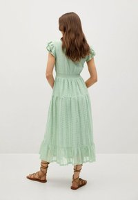 Robe en dentelle vert menthe avec des manches courtes à volants, taille ajustée, jupe à volants et ourlet à volants. Portée avec des sandales brunes à lanières.