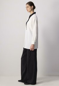 White long-sleeve shirt with a black collar and button cuffs, paired with wide-leg black pants. Smooth fabric texture, minimalist design.