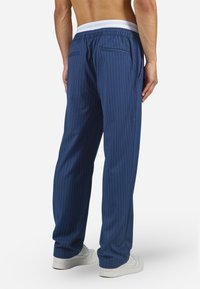 Blauwe gestreepte broek met een witte elastische tailleband, voorzien van twee achterzakken en een relaxte pasvorm, gedragen met witte sneakers.