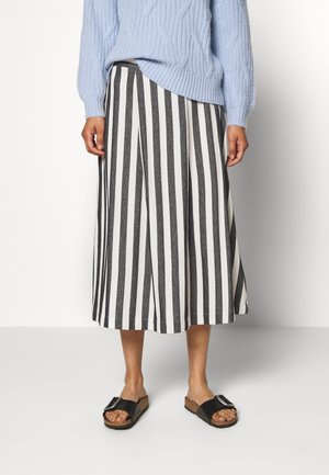 Schwarz-weiß gestreifter, knielanger Rock mit hoher Taille. Kombiniert mit schwarzen Sandalen mit einer großen Schnalle. Hellblau gestrickter Pullover.