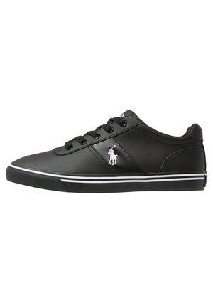Baskets basses noires avec lacets noirs, logo Polo blanc sur le côté et deux fines bandes blanches le long du bord de la semelle.
