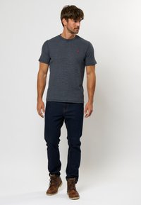 Camiseta de manga corta gris oscuro con tejido texturizado y cuello redondo acanalado; combinada con jeans de mezclilla oscura y botas marrones.