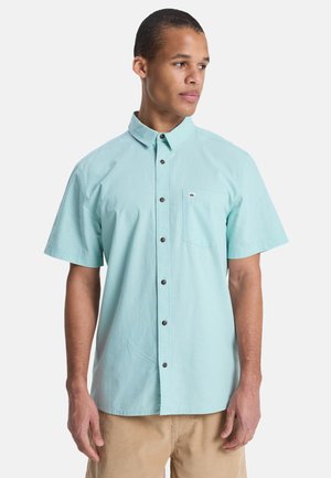 Hellblaues Hemd mit kurzen Ärmeln, Button-Down-Kragen, einer Brusttasche und braunen Knöpfen, aus Baumwolle oder einer Baumwollmischung gefertigt.