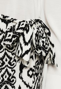 Ύφασμα με ασπρόμαυρο μοτίβο και λεπτομέρεια φιόγκου, με υφή υφαντού και αντίθετη λεία επιφάνεια σε λευκό τοπ.