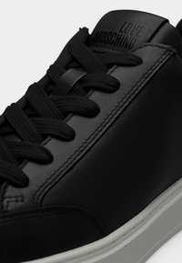 Μαύρο δερμάτινο αθλητικό παπούτσι με μαύρα κορδόνια, λευκή σόλα και την επιγραφή "LOVE MOSCHINO" χαραγμένη στη γλώσσα.