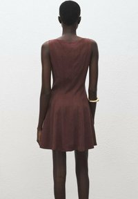 Vestido sin mangas en color marrón burdeos con falda acampanada, hecho de una tela suave. Presenta un escote en la espalda y un sutil patrón de rayas verticales.