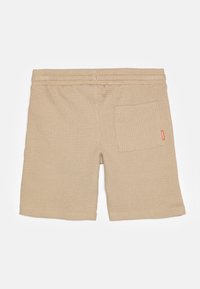 Beige shorts laget av teksturert vaffelstoff. Har elastisk midje og en lomme bak med et lite rødt logo.