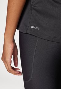 Crni sportski top i tajice s glačanim materijalom, uskim krojem i vidljivim "DRYCELL" logom na rubu. Vidljivi su detalji šavova.