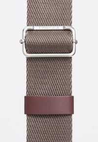 Tkany pasek w stonowanym brązie, z metalową srebrną klamrą i brązowym akcentem o fakturze, podkreślający jego warstwowy design.