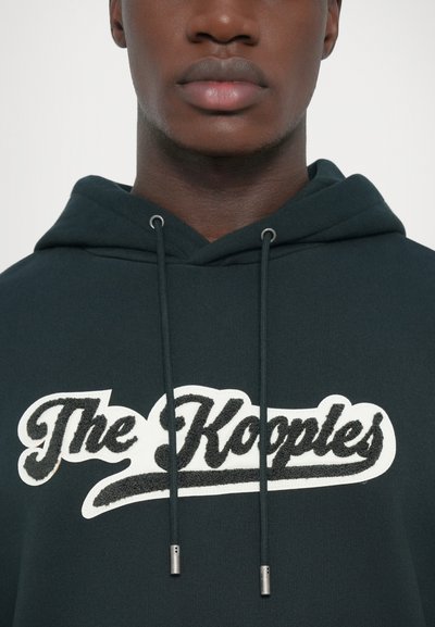 Dark green hoodie featuring a prominent white and black embroidered logo with a textured design. Includes metal-tipped drawstrings.