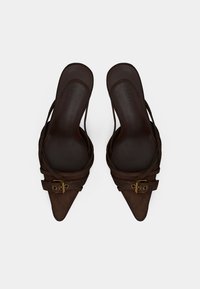 Καστόρινα καφέ παπούτσια με ψηλά τακούνια και μυτερά δάχτυλα, με διασταυρωμένους ιμάντες και χρυσή αγκράφα. Ομαλή εσωτερική επένδυση.