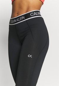 Sorte athletiske leggings med høj talje med en hvid "CALVIN KLEIN"-logo. Blødt, elastisk stof med en glat tekstur.
