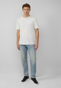 Biała bawełniana koszulka z krótkim rękawem, zestawiona z jasnoniebieskimi dżinsami z przetarciem na kolanie. Czarnie sneakersy dopełniają stylizację.