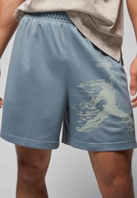 Lyseblå mesh sportshorts med elastisk talje, med et grafisk design på venstre side og en åndbar tekstur.
