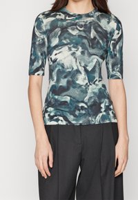 Kortärmad, figurnära topp gjord av ett texturerat tyg i nyanser av teal, vitt och grått med ett virvlande abstrakt mönster.