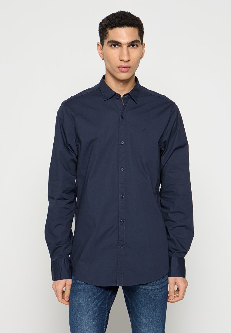 Chemise boutonnière marine avec col, manches longues et design ajusté. Fabriquée en tissu lisse avec une texture subtile. Présente des boutons sur le devant.