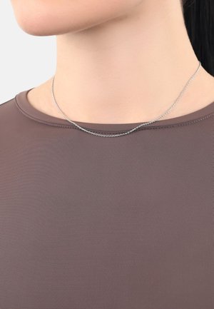 Collana in metallo argentato con un design delicato e sottile, che mostra una texture liscia e una leggera lucentezza su una camicia marrone.