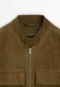 Giubbotto in suede marrone con colletto rialzato, zip frontale e due tasche sul petto. Tessuto morbido con una finitura liscia, senza modelli visibili.