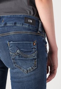 Jeans de mezclilla azul oscuro con bolsillos traseros que presentan un distintivo bordado y una etiqueta de la marca LTB en la cinturilla.