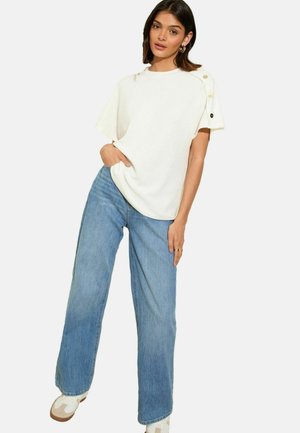 Top bianco a maniche corte con scollatura rotonda e dettagli a bottoni sulle spalle, abbinato a jeans blu in denim larghi. Design semplice e casual.