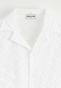 Chemise blanche à manches longues avec un motif texturé comprenant des formes de feuilles cousues. Comprend un collier et une étiquette indiquant "FRILIVIN, taille S."