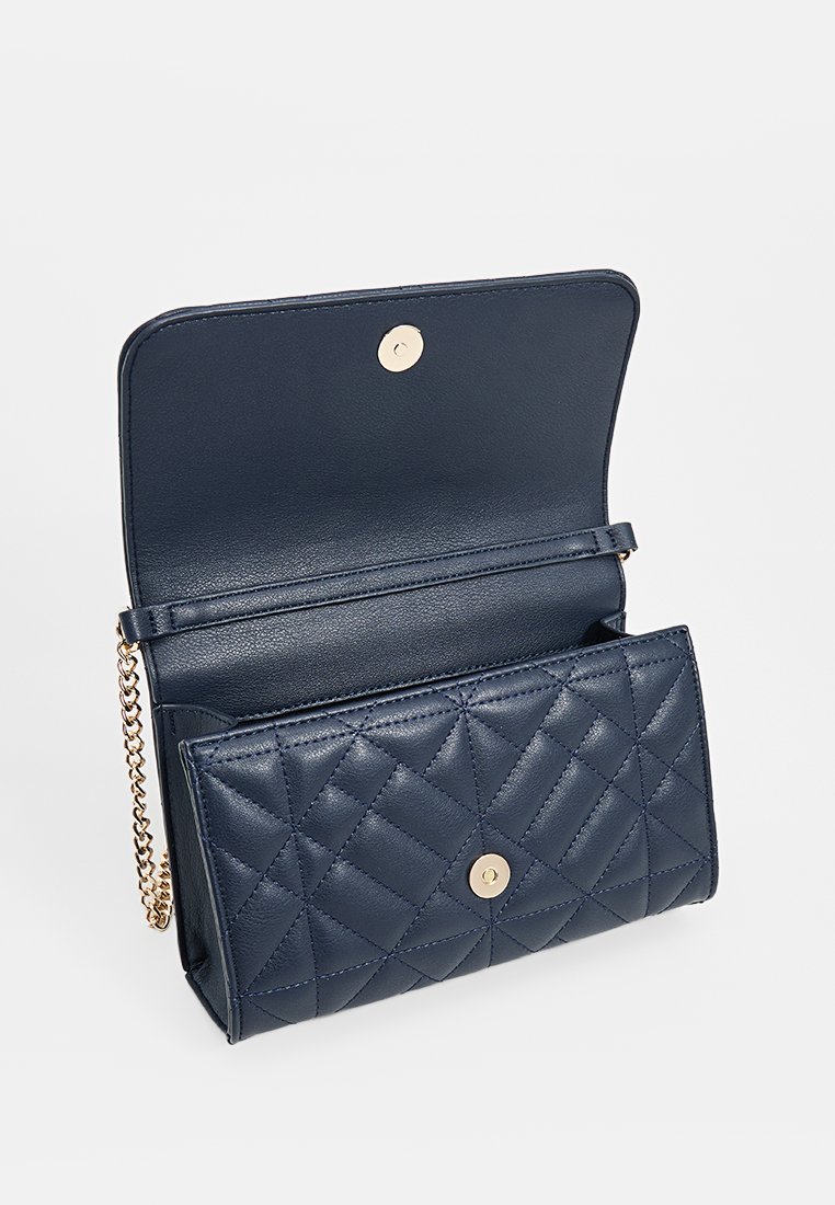 Bolso de mano de cuero azul marino con patrón acolchado, herrajes dorados y correa de cadena. La solapa abierta revela un interior amplio y forrado con un compartimento para tarjetas.