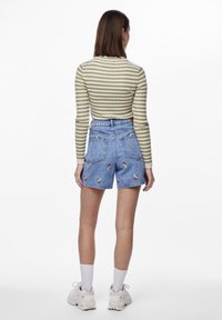 Top de manga larga a rayas en oliva y crema; pantalones cortos de mezclilla de cintura alta con bordado floral; calcetines blancos y zapatillas completan el look.