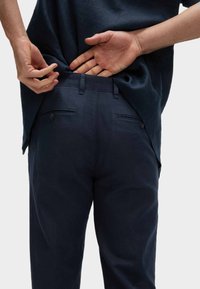 Marineblaues Hosen mit strukturiertem Finish und Gesäßtaschen. Das Modell passt den Stoff des Hemdes über den Bund an. Schlichtes, lässiges Design.