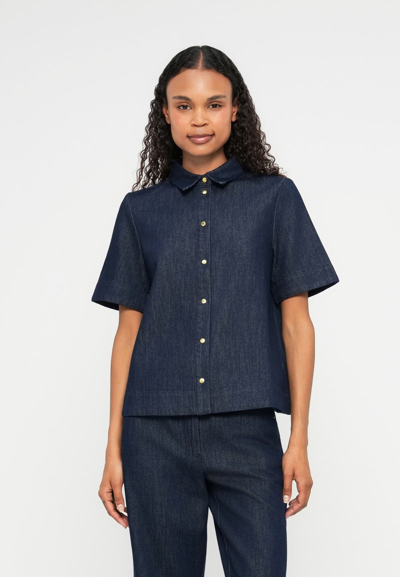 Koszulka krótki rękaw, granatowa z denimu, z kołnierzykiem zapinanym na guziki, z złotymi guzikami i luźnym krojem. Gładka tekstura, casualowy design.