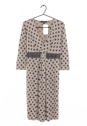 Jasnobrązowa sukienka w czarne grochy, z dekoltem w serek, rękawami trzyczwartowymi i czarnym paskiem w grochy. Wisi na czarnym wieszaku.