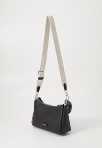 Sac en cuir noir texturé de forme trapézoïdale, avec des accessoires en métal argenté et une bandoulière beige amovible. Fermeture zippée, petit accent sur le côté.