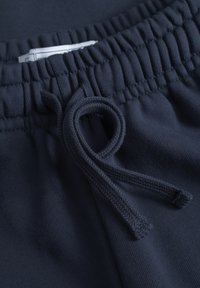 Navyblaue Jogginghosen mit elastischem Bund und Kordelzug. Der Stoff ist weich und hat eine gerippte Textur. Das Etikett ist teilweise im Bund sichtbar.