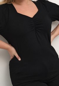 Haut noir à manches courtes avec un col en V et un détail de tissu froncé au centre. Confectionné en matière douce, il présente une coupe décontractée.