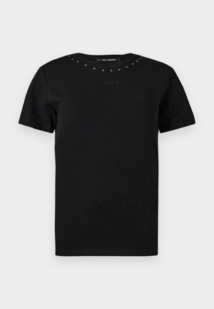 Camiseta negra de manga corta con cuello redondo, pequeños tachuelas metálicas a lo largo del cuello y una sutil firma bordada en el pecho.