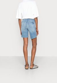 Pantalones cortos de denim azul claro con corte recto, cintura a media altura y dos bolsillos traseros. Combinados con una camiseta blanca holgada y sandalias grises.