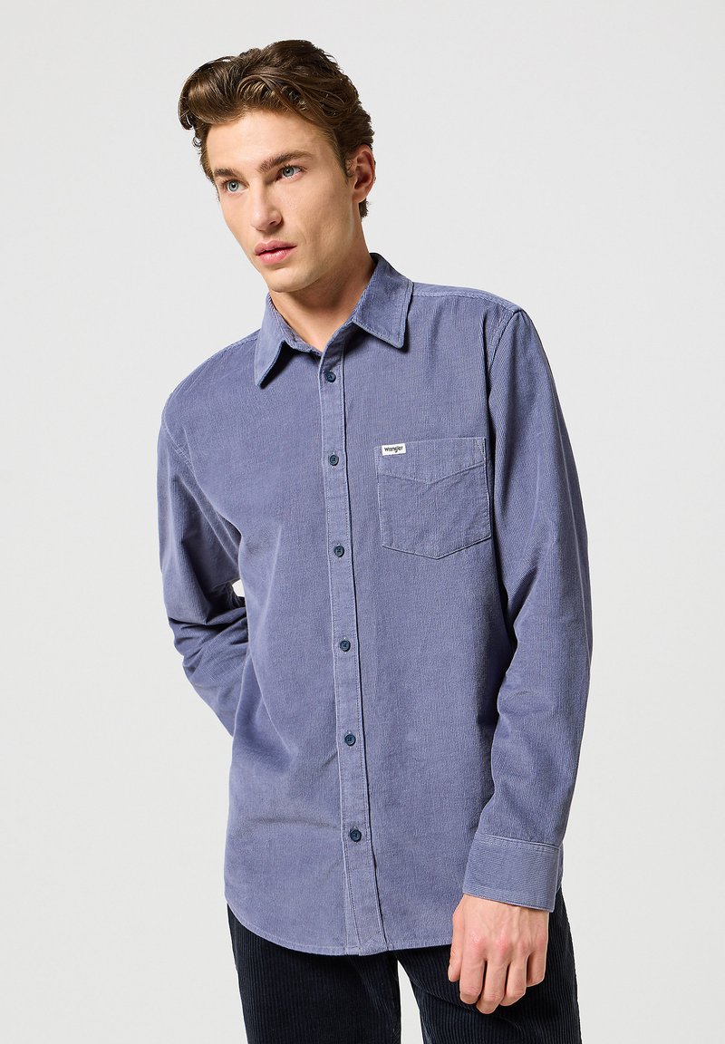 Camisa de manga larga, con botones, en tejido de pana azul oscuro. Cuenta con un bolsillo en el pecho, botones en contraste y un collar de tipo solapa.
