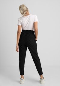 Pantalons noirs à rayures avec une taille élastique, associés à un t-shirt rose clair. Le modèle porte des baskets blanches. Design simple, forme ajustée.