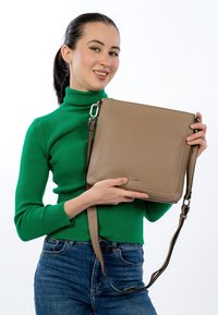 Tan leather crossbody bag with a textured finish, featuring a slim shape, adjustable strap, and stitching accents.