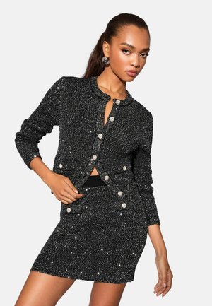Black sparkly knit outfit featuring a fitted cardigan with pearl buttons and a matching mini skirt adorned with shiny accents.