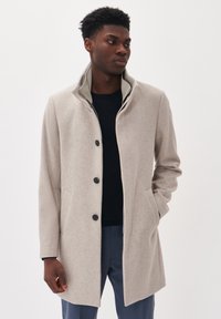 Abrigo de lana gris claro con un alto cuello, cuatro botones y dos bolsillos laterales. Textura suave, corte ajustado y un detalle sutil en el cuello.