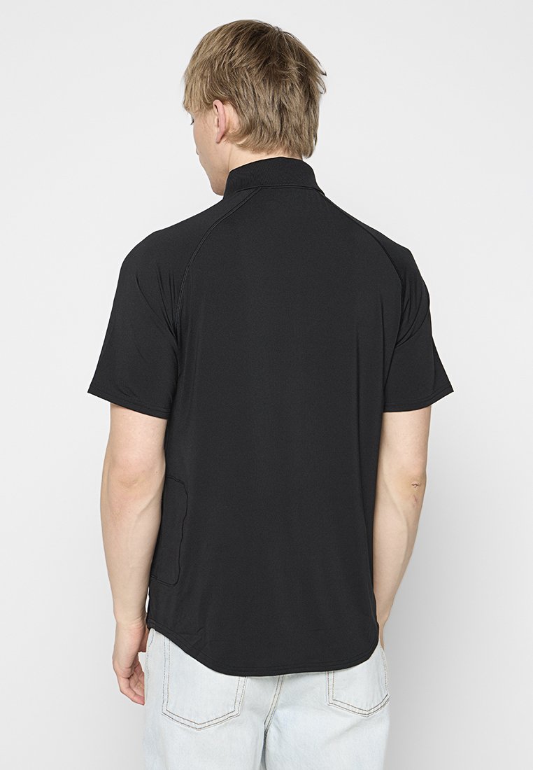 Schwarzes Kurzarmhemd mit Kragen, glatter Textur und abgerundetem Saum. Mit seitlicher Taschenmöglichkeit. Die Rückansicht ist dargestellt.